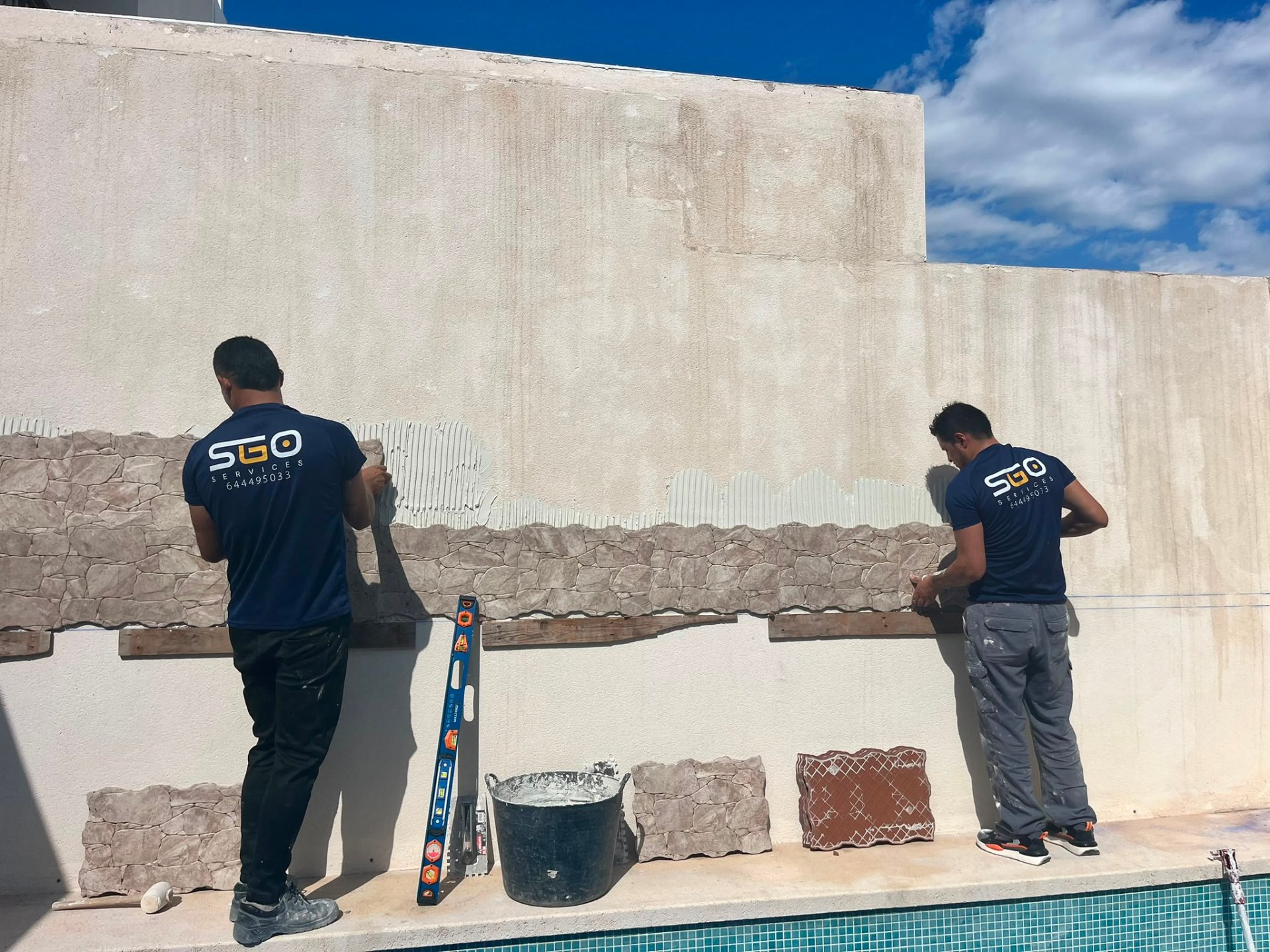 Equipo de SGO Services colocando revestimiento de piedra en un exterior con piscina